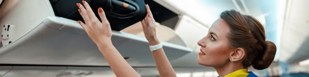 Woman flight attendant or air hostess placing travel bag in overhead baggage locker while standing in airplane passenger salon